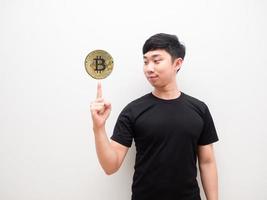 asiatischer mann schaut sich gold bitcoin an seinem finger oben rechts auf weißem isoliertem hintergrund an kryptogeldkonzept foto