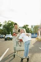 Glückliche Mutter und ihre Töchter haben Spaß mit einem Einkaufswagen auf einem Parkplatz neben einem Supermarkt. foto