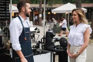 Barista-Mann und seine Kundin unterhalten sich an Sommertagen neben dem Café. foto