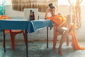 Stilvolle Frau in schönem orangefarbenem Kleid, die in der alten authentischen Cafeteria sitzt foto