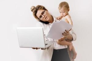 Junge und beschäftigte Geschäftsfrau arbeitet und hält ihr kleines Baby foto