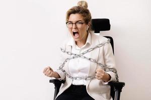 Wütende Geschäftsfrau, die mit Ketten an den Bürostuhl gefesselt ist foto