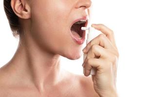 Frau verwendet Spray mit Analgetikum zur Linderung von Halsschmerzen foto