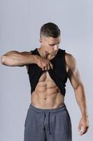 junger Bodybuilder, der seinen muskulösen Körper vor grauem Hintergrund zeigt foto