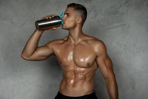 Bodybuilder, der Molkenprotein oder andere Nahrungsergänzungsmittel aus einem Metallshaker trinkt foto