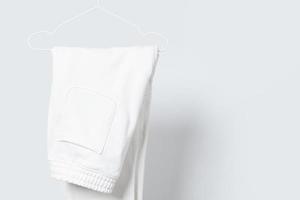 leere weiße Jogginghose, die auf einem Kleiderbügel vor grauem Hintergrund hängt foto