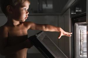 Neugieriger kleiner Junge öffnet den heißen Ofen. Sicherheitskonzept und mögliche Probleme mit unbeaufsichtigten Kindern. foto