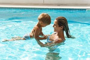 Mutter und ihr süßer kleiner Sohn schwimmen während der Sommerferien im Außenpool foto