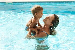 Mutter und ihr süßer kleiner Sohn schwimmen während der Sommerferien im Außenpool foto