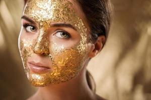 schöne frau mit goldglänzender maske auf ihrem gesicht zur hautbehandlung