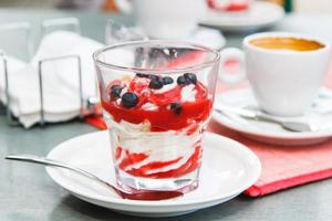 Glas Eisdessert mit Heidelbeeren und Sirup auf dem Café-Tisch. foto