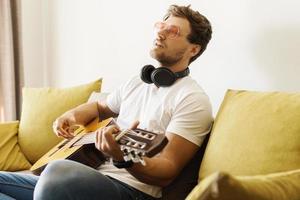 Junger Mann auf dem Sofa spielt Akustikgitarre foto