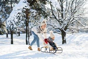 mutter und ihr süßer kleiner sohn haben an einem sonnigen wintertag auf einem rodelhügel foto