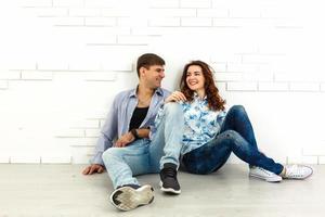 Der glückliche Mann und die glückliche Frau sitzen auf dem Hintergrund der weißen Wand foto