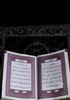 al-Quran, der sich über dem Gebetsteppich mit schwarzem Hintergrund befindet foto