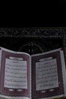 al-Quran, der sich über dem Gebetsteppich mit schwarzem Hintergrund befindet foto