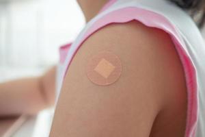 Geimpftes kleines asiatisches Mädchen mit Heftpflaster nach der Impfinjektion foto