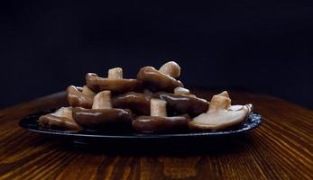 Ein Haufen eingelegter Pilze in einem schwarzen Teller auf einem Holztisch. Gesundes Dorfessen. foto