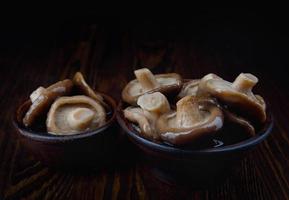 Auf einem Holztisch stehen köstlich eingelegte Pilze in Tonbechern. gesalzene Pilze. rustikales essen. foto