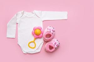 Bodysuit für ein Neugeborenes, Rassel und Schühchen auf rosafarbenem Hintergrund mit Copyspace foto