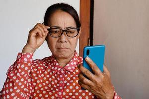 asiatische Seniorin hat Probleme mit dem Sehvermögen beim Betrachten des Smartphones, hält eine Brille. Konzept, Heideproblem foto