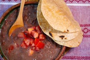 bohnen gekocht in einem lehmgericht mit tomaten und tortillas, mexikanisches armes gericht foto