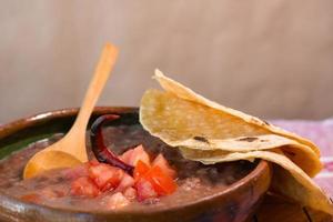 bohnen gekocht in einem lehmgericht mit tomaten und tortillas, mexikanisches armes gericht foto