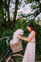 junge frau, die weißen bichon frise hund in den korb des elektrofahrrads legt foto