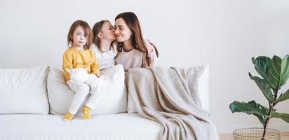 junge glückliche familie mit einer elternfrau mutter mit zwei kindern mädchen auf der couch im wohnzimmer mit grüner hauspflanze zu hause foto