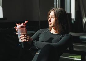 porträt einer ruhenden jungen brünetten frau im sportbekleidungs-trinkwasser im fitnessclub-fitnessstudio foto