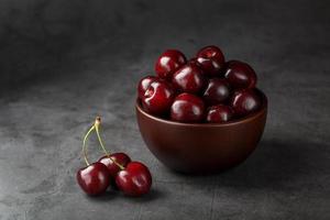 Reife und saftige Kirschbeeren auf einem schwarzen strukturierten Hintergrund in einer braunen Tasse mit Wassertropfen. Draufsicht, Nahaufnahme. foto