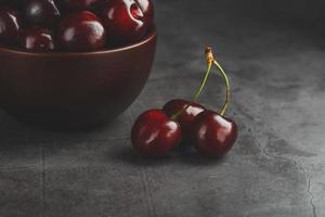 Reife und saftige Kirschbeeren auf einem schwarzen strukturellen Hintergrund in einer braunen Tasse mit Wassertropfen. Draufsicht, Nahaufnahme, Makro. foto