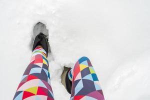 schlanke weibliche Beine in leuchtend bunten Leggings und warmen wasserdichten Stiefeln stehen an einem frostigen Wintertag in einer tiefen Schneeverwehung. Lebensstil. foto