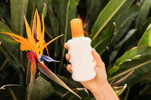 Nahaufnahme einer Frau, die eine Flasche Hautpflegeprodukt in der Nähe der tropischen Blume hält. foto