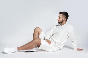 Gutaussehender Mann mit weißem Sweatshirt und Shorts mit drahtlosen Ohrstöpseln im Sitzen foto