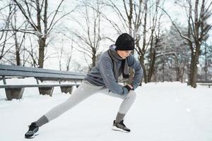 athletische frau, die sich vor ihrem joggingtraining während des verschneiten wintertages in einem stadtpark aufwärmt foto