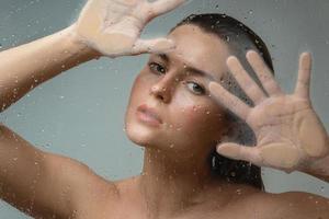 Porträt einer sinnlichen Frau, die durch nasses Glas eingefangen wurde foto