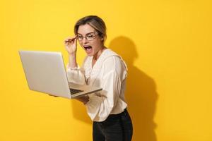 Fröhliche Frau mit Brille benutzt Laptop-Computer auf gelbem Hintergrund foto