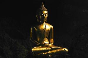 Bronze-Buddha-Statue, die in Lotus-Pose in einer Höhle betet. foto