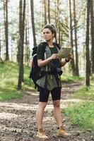 Wanderin mit großem Rucksack mit Karte für Orientierungslauf im Wald foto