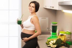 glückliche schwangere Frau, die gesunden grünen Smoothie trinkt foto