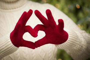 Frau mit roten Fäustlingen, die ein Herz-Handzeichen hält foto