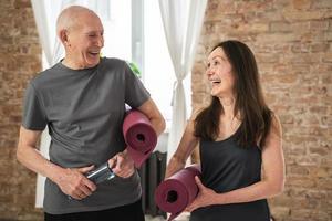 zwei fröhliche und aktive alte menschen mit trainingsmatten, die zum training bereit sind foto