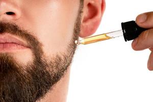 männliches Gesicht und Pipette mit einem Öl für einen Bartwuchs foto