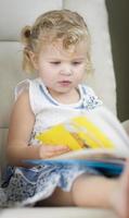 blondes blauäugiges kleines Mädchen, das ihr Buch liest foto