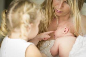 junge mutter hält neugeborenes mädchen, während junge schwester aussieht foto