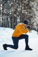 sportlicher Mann, der während seines Wintertrainings im verschneiten Park Ausfallschritte macht foto