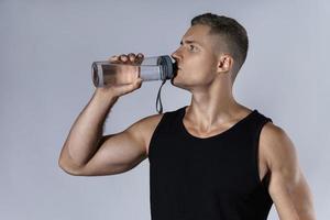 Trinkwasser des sportlichen Mannes gegen grauen Hintergrund foto