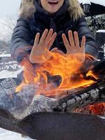 Frau, die ihre Hände an der Feuerstelle aufwärmt foto