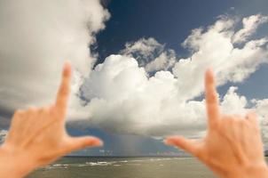 Hände, die dramatische Wolken über der tropischen Küste einrahmen foto